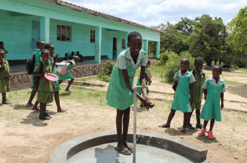 Smiling school girl in green uniform washes her hand at the new water point