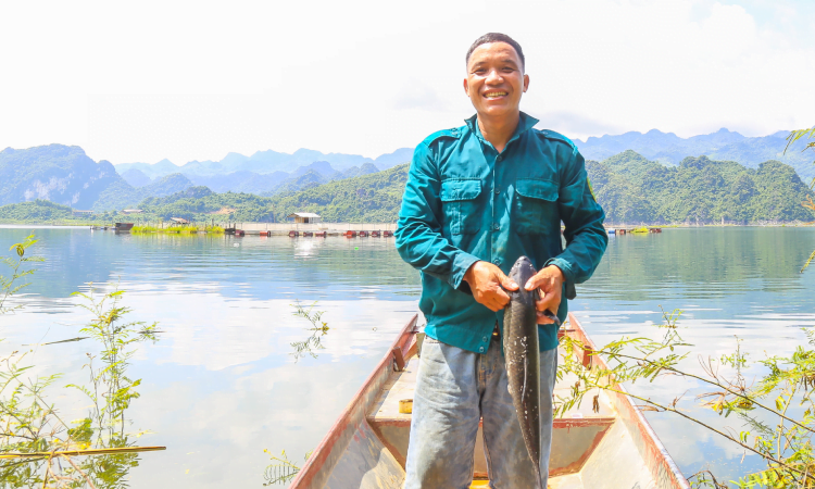 Mr Duy with a fish, with view of a boat and lake behind him