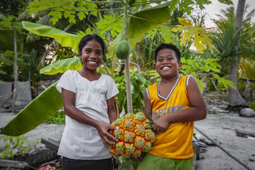 Smiling girl and boy hold fruit in Kiribati - Action on Poverty