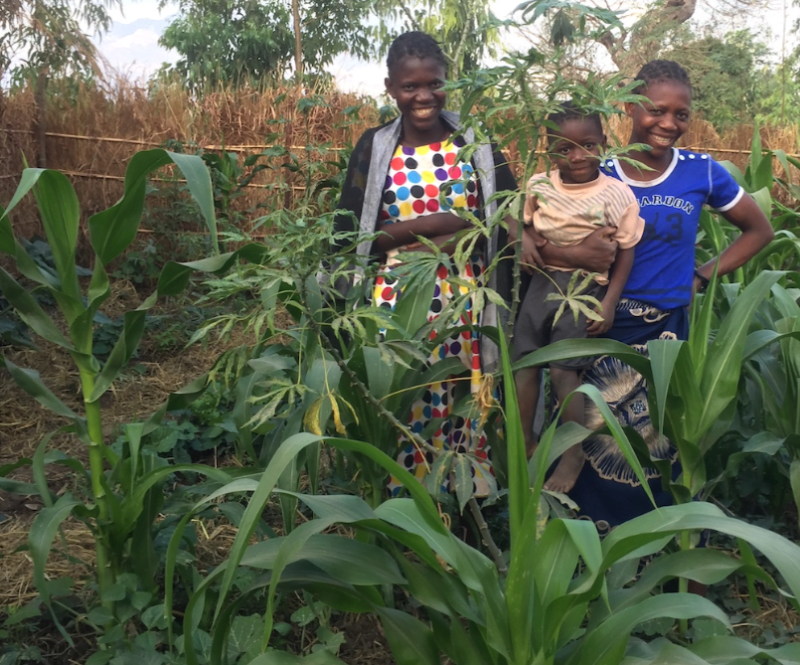 Two smiling women and baby standing in their victory garden in Malawi - Action on Poverty