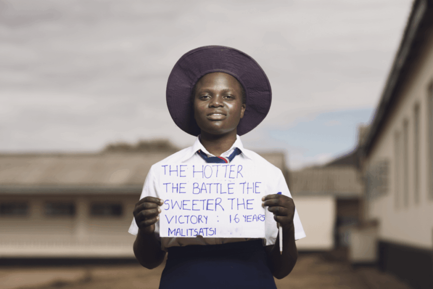 Malitsatsi in school uniform, holding a sign that says: 'The hotter the battle, the sweeter the victory.'