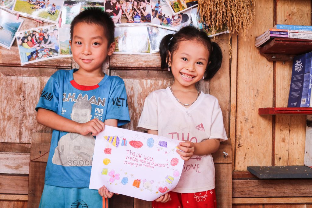 Smiling Vietnamese boy and girl hold a hand-drawn sign that says 'thank you' in Vietnamese